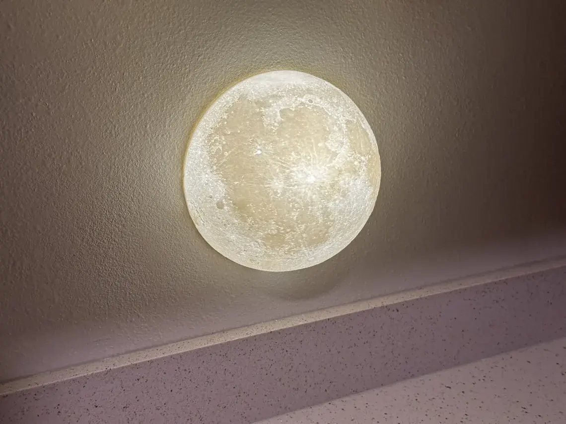 The Smart Plug Ready moon night light lit on a wall above a kitchen counter, spilling a warm circle of light onto the wall around it